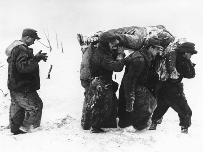 German prisoners of war are seen as they carry the body of an American soldier through deep snow, during the Battle of the Bulge, in the Ardennes sector of Belgium, in late 1944.