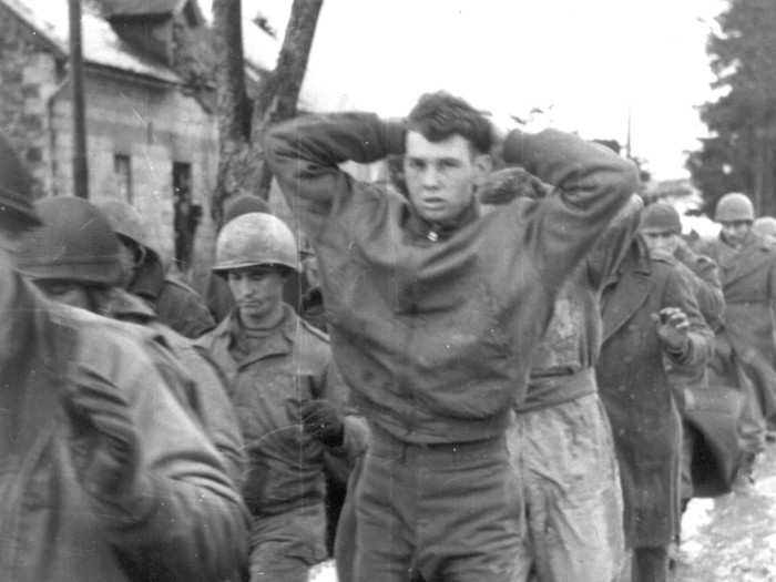 An unidentified young American soldier, captured by German troops during their counterattack in the Belgian Ardennes region, leads a march of prisoners at an unknown location in December 1944.