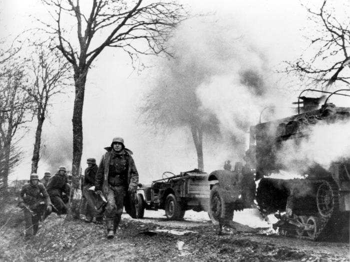 German infantrymen pass burning captured American vehicles during the drive into Allied lines on the Western Front in the Battle of the Bulge in December 1944 during World War II. This photo is from a batch of film captured from the Germans by American forces.