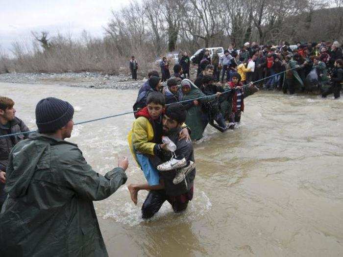 Refugees and migrants form a human chain to cross a river near the Greek-Macedonian border, west of the the village of Idomeni, Greece, on March 14.
