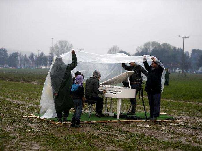 Chinese dissident artist Ai Weiwei holds a rain cover to protect a Syrian refugee woman from the rain as she performs in a field on a piano brought by the artist, near a makeshift camp on the Greek-Macedonian border on March 12.