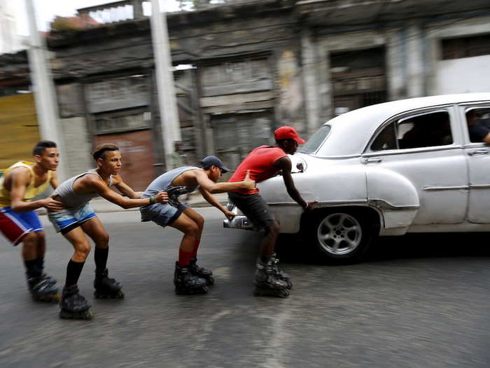 Teenagers on roller skates held on to each other as they were pulled by a vintage car in Havana, Cuba.