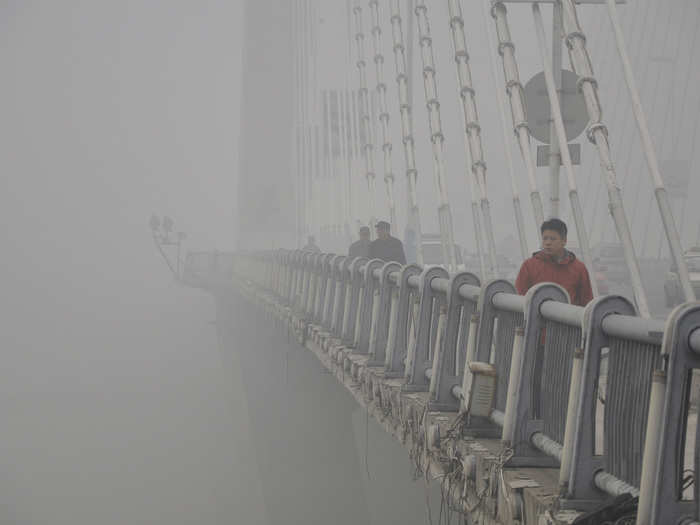 Citizens walk across a bridge, their line of sight extremely short due to the thick smog.