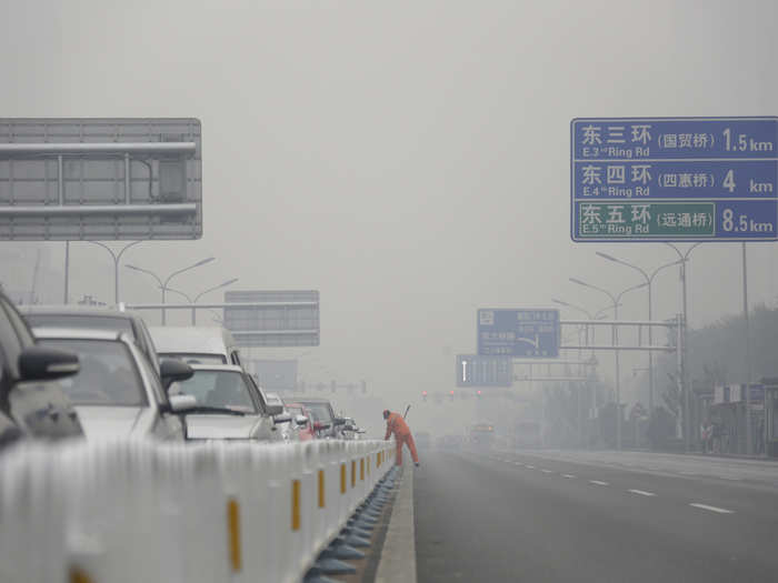 Despite the poor air quality, cleaners work along the median of a main road in central Beijing.