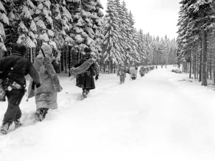 Troops of the 82nd Airborne Division travel a snow-covered fire break in the woods as they move forward in the Ardennes region in Belgium, on January 28, 1945.