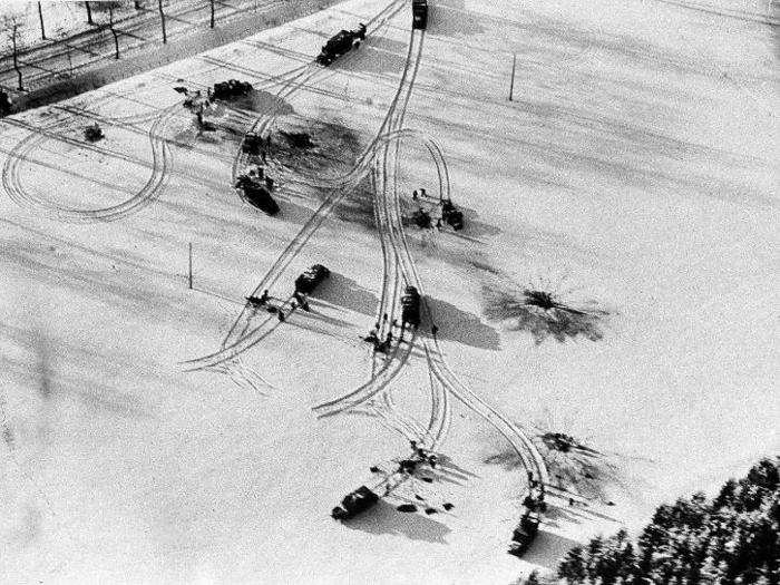 The vehicles of an Allied platoon halt in a snow-covered field in the Ardennes area of Belgium, striped with wheel tracks and splotched with blackened shell craters, January 27, 1945.