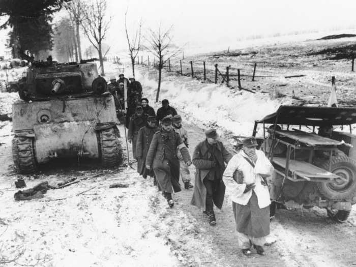 German captives walk past a disabled tank as they are led into captivity by US troops, on January 25, 1945, north of Foy, Belgium, in the final days of the Battle of the Bulge.