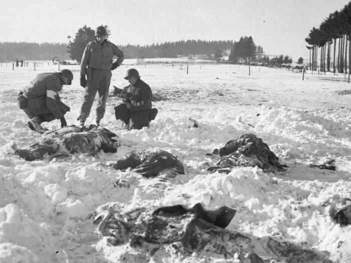 American soldiers check for identification on the bodies of dead US troops shot by the Germans near Malmedy, Belgium, during World War II