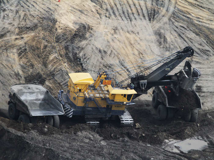 Trucks and shovels move in to scoop up the oil sand — this shovel is electric — and scoops up 90 tons in one load. It takes about 2.5 tons of sand to produce one barrel of oil.