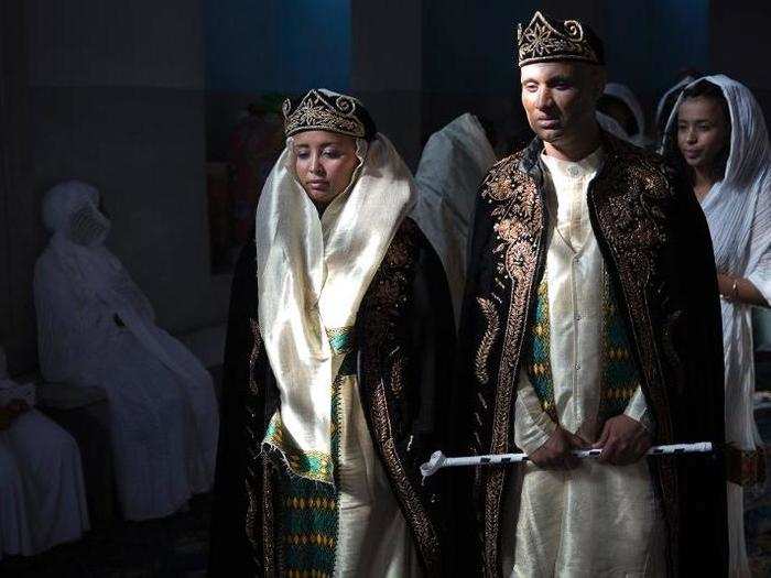 Traditional Eritrean wedding attire includes dark-colored velvet crowns and robes in purple and gold. The bride matches her soon-to-be husband.