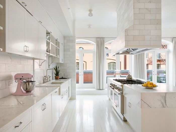 The pink KitchenAid mixer, a plate of lemons, and a small plant provide the only pops of color in the monochromatic kitchen.