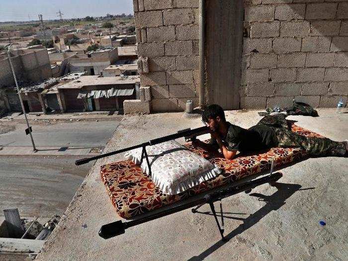 An SDF sniper scans the road below as he lays in an elevated position.