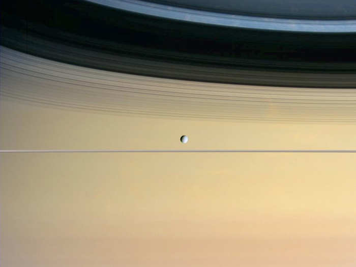 Dione, a small icy moon, is dominated by Saturn and its ring shadows in this image.