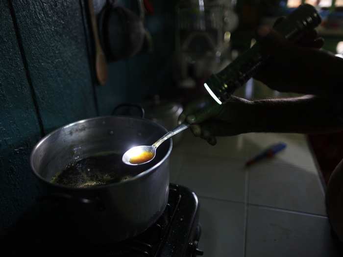 Gonzalo illuminates a spoonful of liquid coca paste with a flashlight as he cooks it to remove the water content, working in the kitchen of his home. He uses the flashlight because there is no electricity in his house.