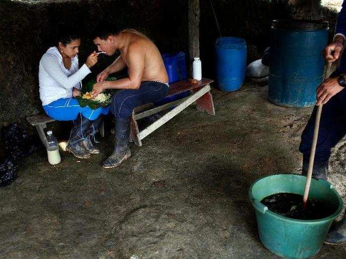 Valeria and her husband share a plate as they eat lunch near a laborer stirring a concoction of coca-leaf extract and cement mixed with gasoline. Noxious fumes emanating from the mixture are a normal part of the manufacturing process.