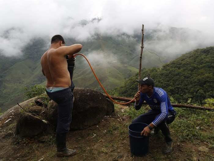 A laborer siphons gasoline as Edgar, left, holds a bucket during the production of coca paste. Coca leaves are mixed in big vats that contain gasoline, ether, and other chemicals into a kind of yellow brew.