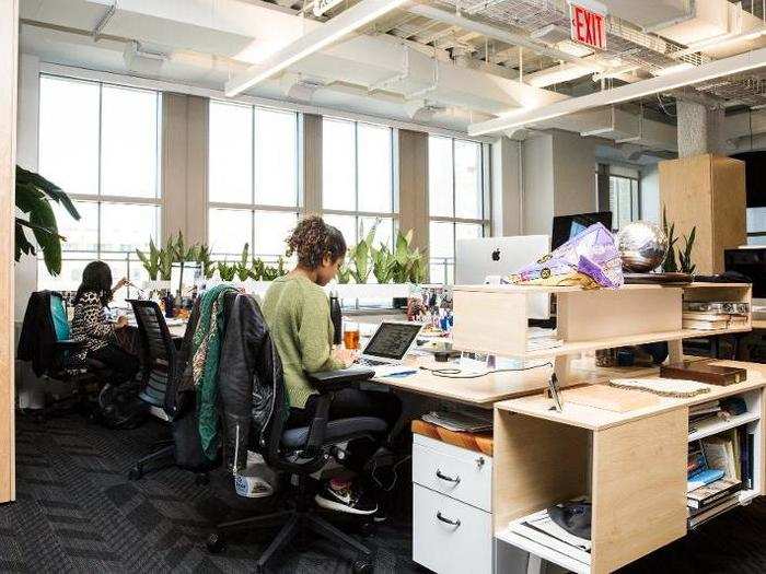 The open-plan office was designed to give people flexibility in how they work. Some people using standing desks, while others have no desk at all — instead, they rely on love seats with swivel work trays. Tiny plants separate each desk.