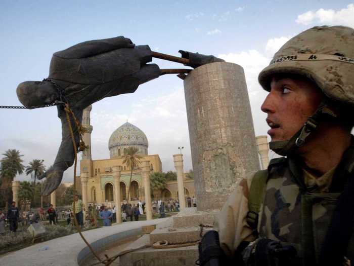 In this iconic photo, a Marine looks on as a statue of Saddam Hussein is pulled down in central Baghdad