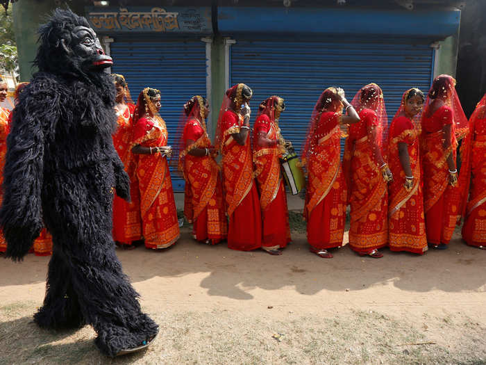 A performer dressed in a chimpanzee costume walks past brides as they arrive at a mass marriage ceremony in which, according to its organizers, 109 tribal, Muslim, and Hindu couples from various villages across the state took their wedding vows, at Bahirkhand village, north of Kolkata, India.