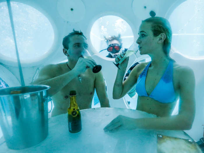 A couple drinks champagne while sitting inside "The Pearl," a spherical dining room placed 5 meters underwater in the NEMO33 diving center — one of the world