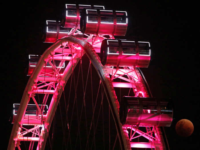 In this image from Singapore, the reddish eclipsed moon (bottom right) is contrasted against the pink lights of a Ferris wheel.