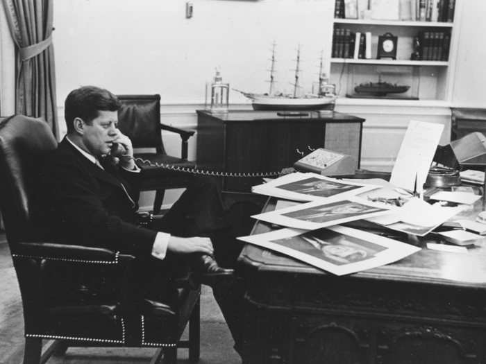 John F. Kennedy was in the process of redesigning the Oval Office when he was assassinated. The idea was to install a new red rug and pale curtains. In terms of furniture, Kennedy added a rocking chair, white sofas, and replaced the sconces with brass lantern. The sailing enthusiast also displayed paintings of naval battles, photos of sailboats, and ship models.