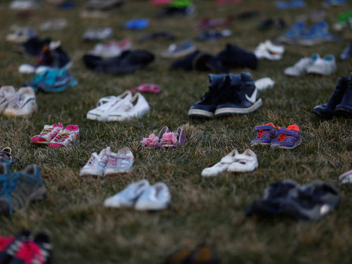 Dozens of activists stood in front of the shoes on Tuesday, holding signs with slogans like "#NOTONEMORE" and "7000 KIDS KILLED"