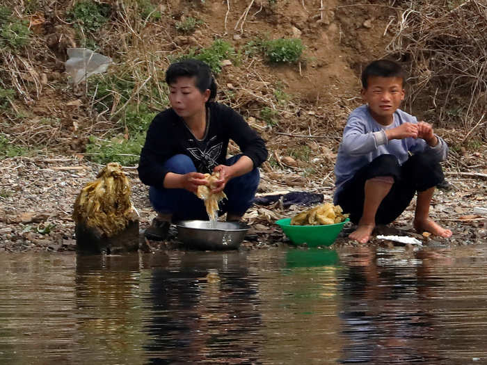 The North Korean woman and child are washing vegetables in river water along the bank of the Yalu.