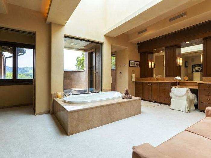 The master bathroom includes a large tub with a skylight overhead, as well as a couch and a vanity.