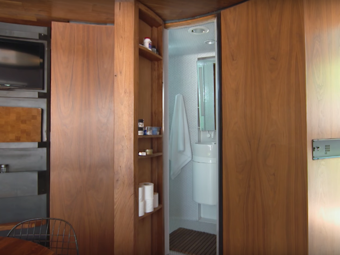 Right next to the kitchen is the bathroom, hidden away behind a tall cabinet door that blends into the wall.