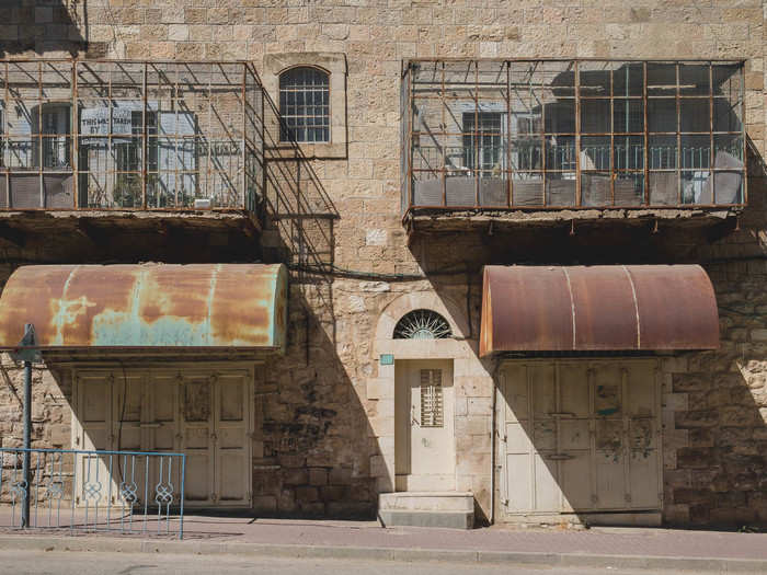 The sign attached to the left balcony in this image reads, "Caution: This was taken by Israel. You are entering Apartheid." Though Palestinians live in these buildings, they are not allowed to walk on this street and must instead climb over roofs to reach their homes. The fencing around the balconies was constructed to protect residents from settlers throwing stones.