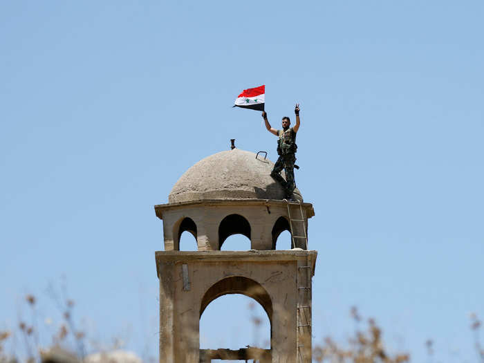 A Syrian army soldier gestures as he holds a Syrian flag in Quneitra, Syria July 27, 2018.