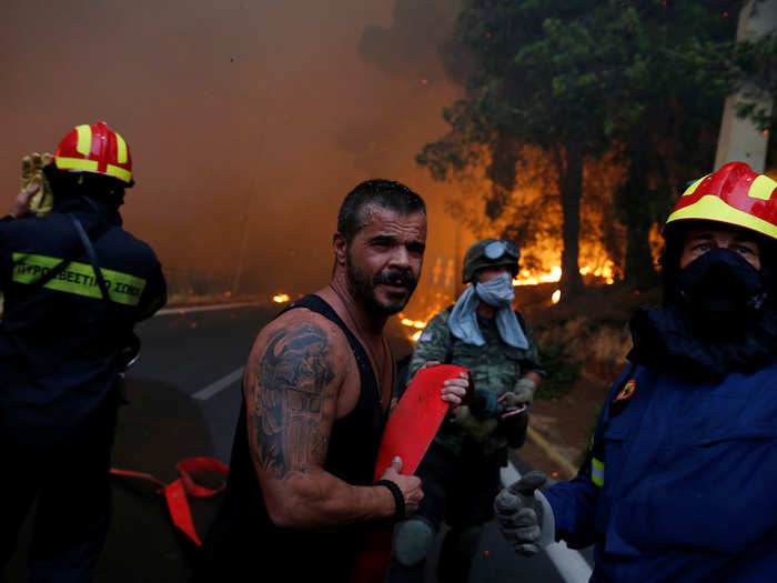 Firefighters, soldiers and local residents carry a hose as a wildfire burns in the town of Rafina, near Athens, Greece, July 23, 2018.