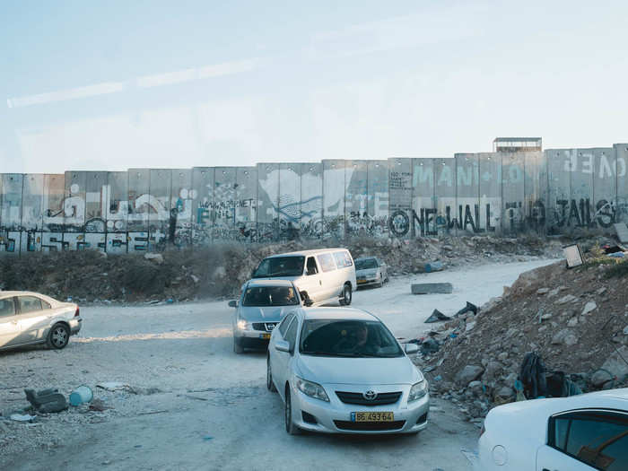 The 30-foot wall of solid concrete is covered with graffiti. In most areas, it is topped with coils of razor wire. The graffiti on the right reads "One Wall, Two Jails."