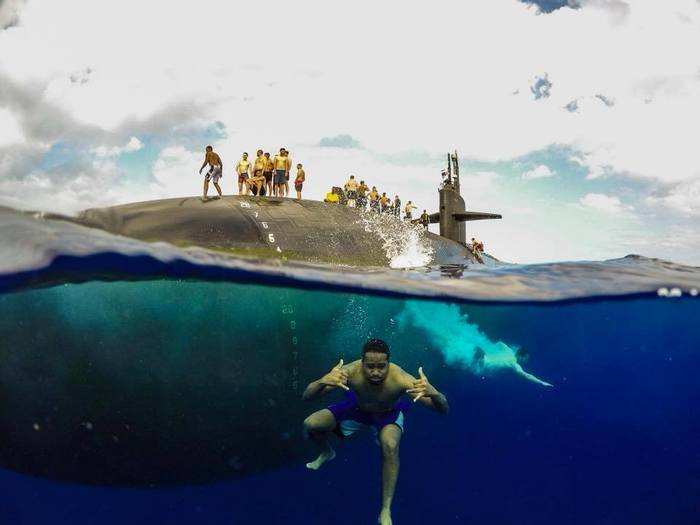 A sailor serving on the Olympia gives a shaka sign, a gesture from Hawaiian surf culture, to the camera.