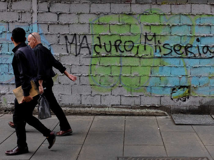 People walk past a graffiti that reads: "Maduro, misery"