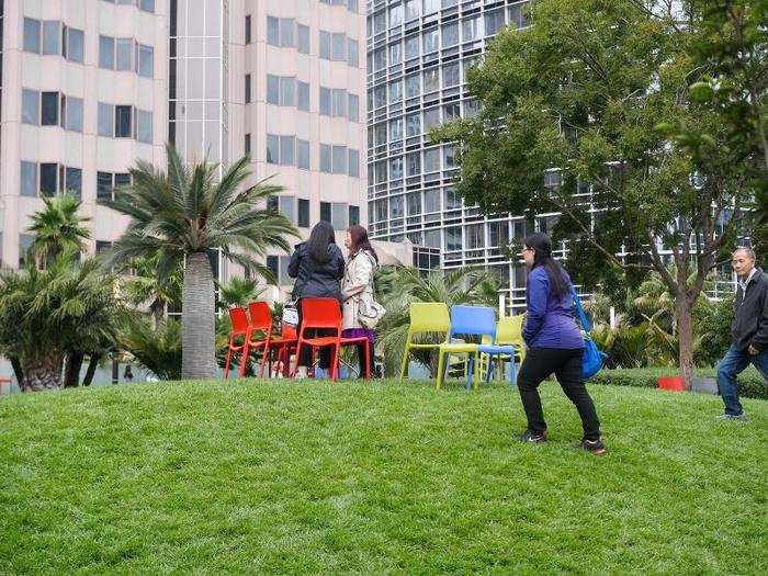 A spacious lawn runs the length of the park, with moveable chairs and tables for people to use.