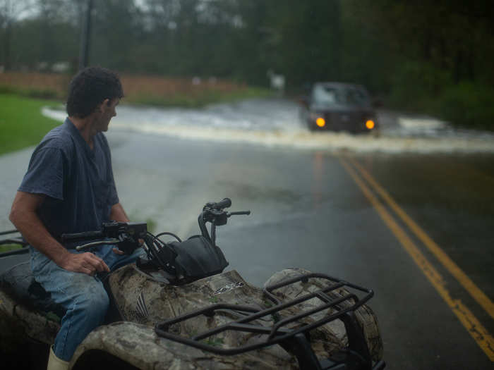 A man named Kenny sits watches a pickup truck pass through a heavily flooded road, which almost rose above the vehicle