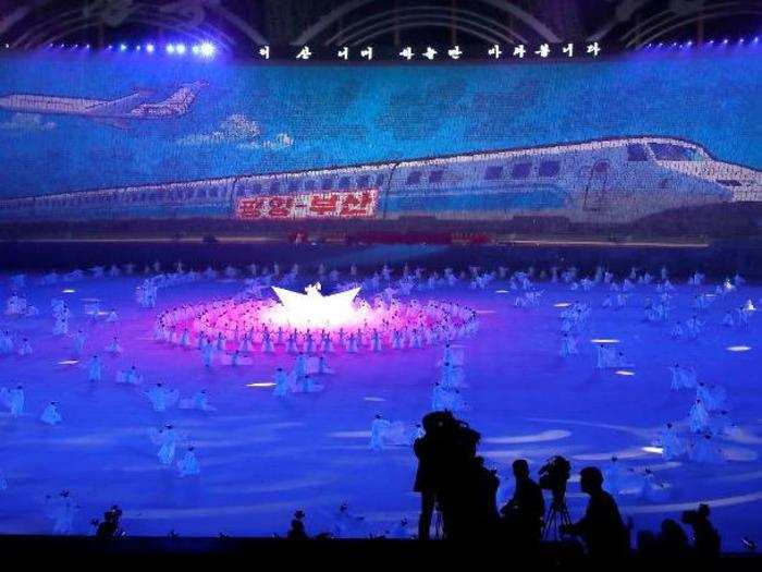 Thousands of choreographed cards display a massive image of a train that says "Pyongyang — Pusan." Pusan is a coastal city in South Korea.