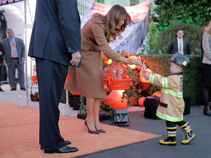 Standing next to the President, the First Lady greeted a miniature firefighter with a treat from her basket on Halloween 2017.