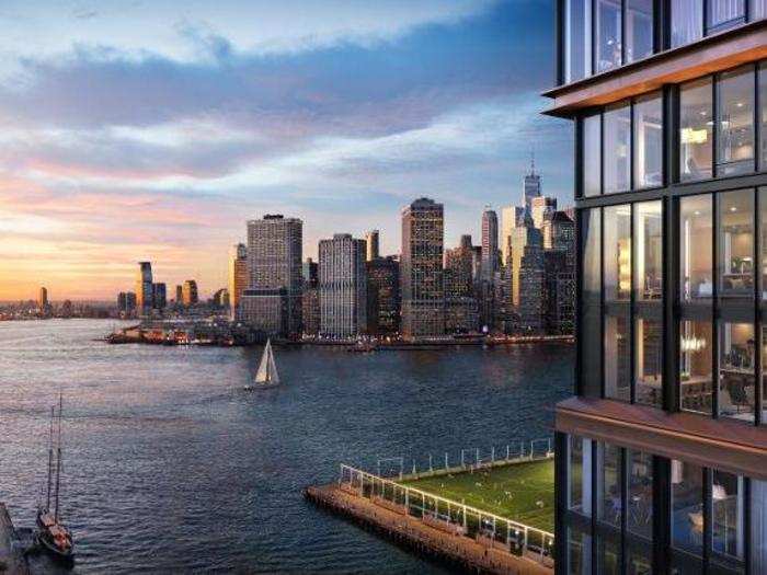 The penthouse features floor-to-ceiling windows, from which the Manhattan skyline, Brooklyn Bridge Park, and the Statue of Liberty are all visible.