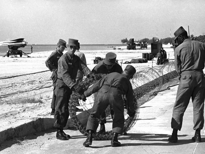 US troops string barbed wire along the Key West shore facing Havana, November 1, 1962. Military installations, rushed in during the Cuban missile crisis, line the beach in the background.