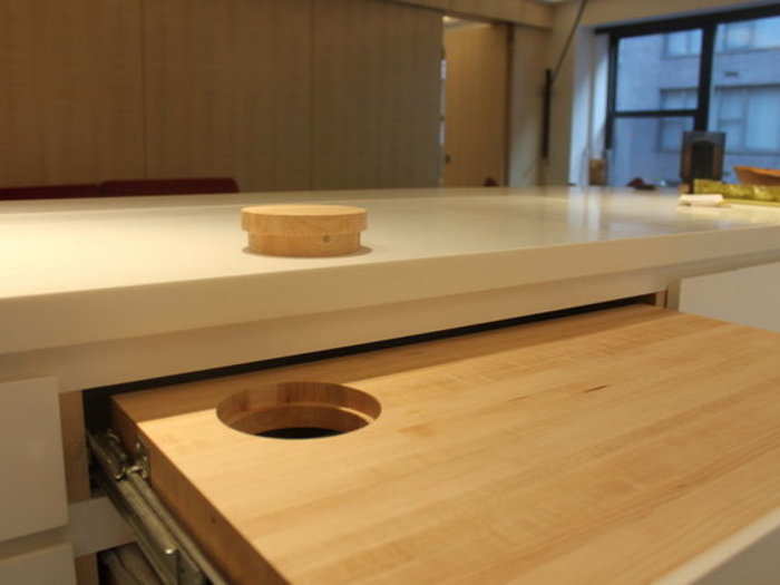 A pull-out cutting board has a hole for disposing of scraps in the trash can below.