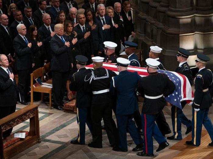 Mourners, including President Trump, pay their respects as the flag-draped casket of former President George H.W. Bush is carried by a military honor guard.