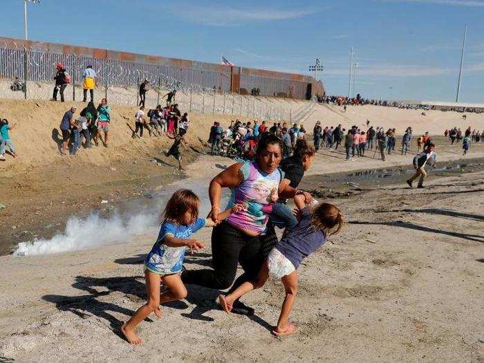 A migrant family, part of a caravan of thousands traveling from Central America to the U.S., runs away from tear gas in front of the border wall.