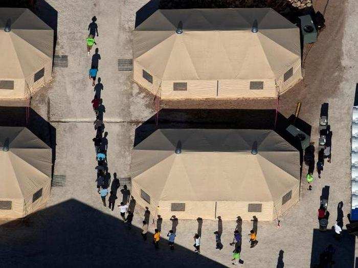 Immigrant children are led by staff in single file between tents at a detention facility near the Mexican border.