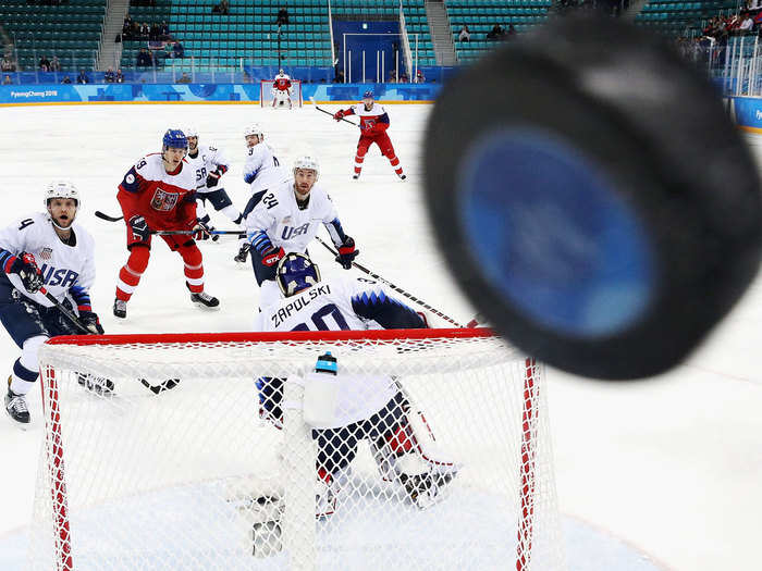 Hockey players from the Czech Republic and the United States watch as the puck sails over the net and into the glass at the 2018 PyeongChang Olympics.