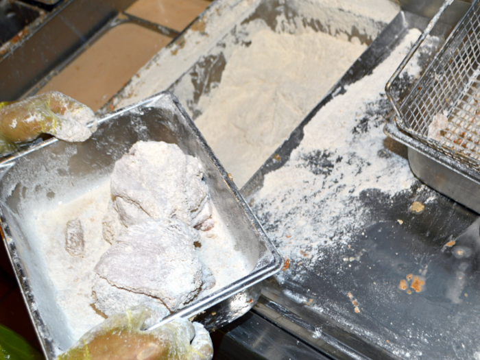 Fillets get flipped over, covered, and pressed down again for an even coating. Then they go into one of two bins dedicated to the original chicken, and move onto the fryer.