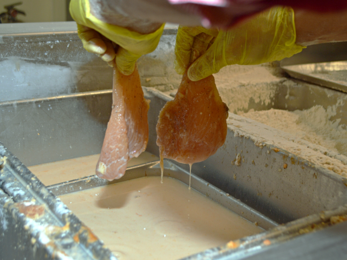 After the ones that make the cut are filleted properly, breaders hold onto the chicken by the tail — two at a time — and dunk them in the milk and egg wash just once.