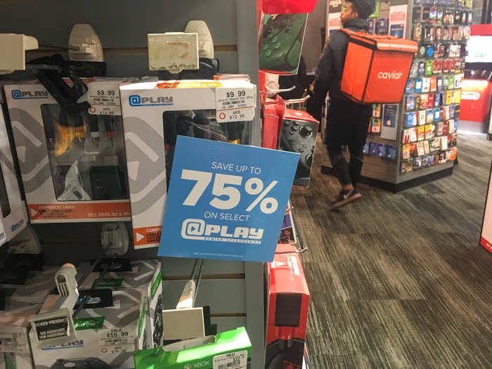 A sign promoting 75% savings on gaming accessories, like a universal component cable, was displayed next to the @Play products.